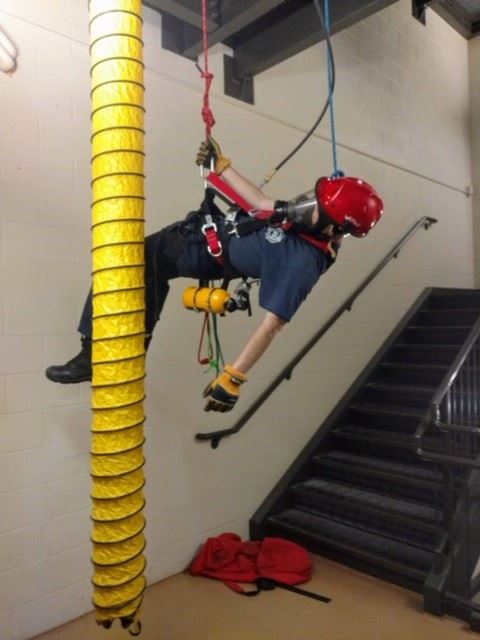 fireman hanging from ropes simulating rope rescue by yellow air tube